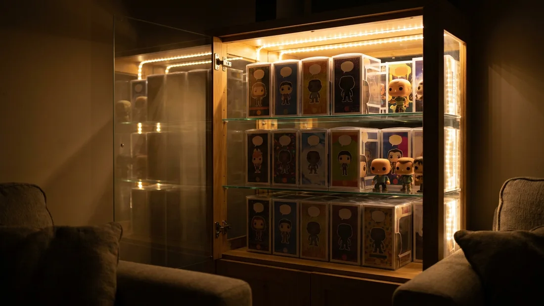 Vitrine en verre éclairée la nuit avec des boîtes de figurines collector protégées rangées par thème